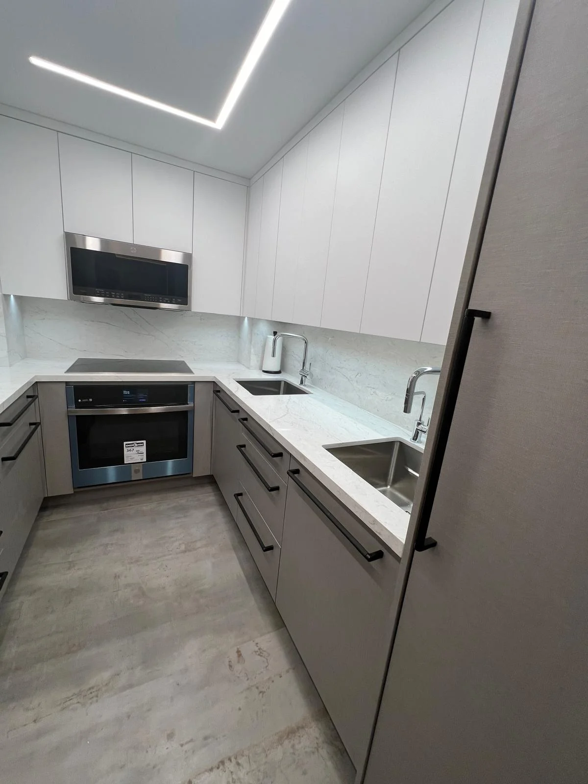 Modern white kitchen with quartz counters, stainless steel appliances, and LED ceiling lights