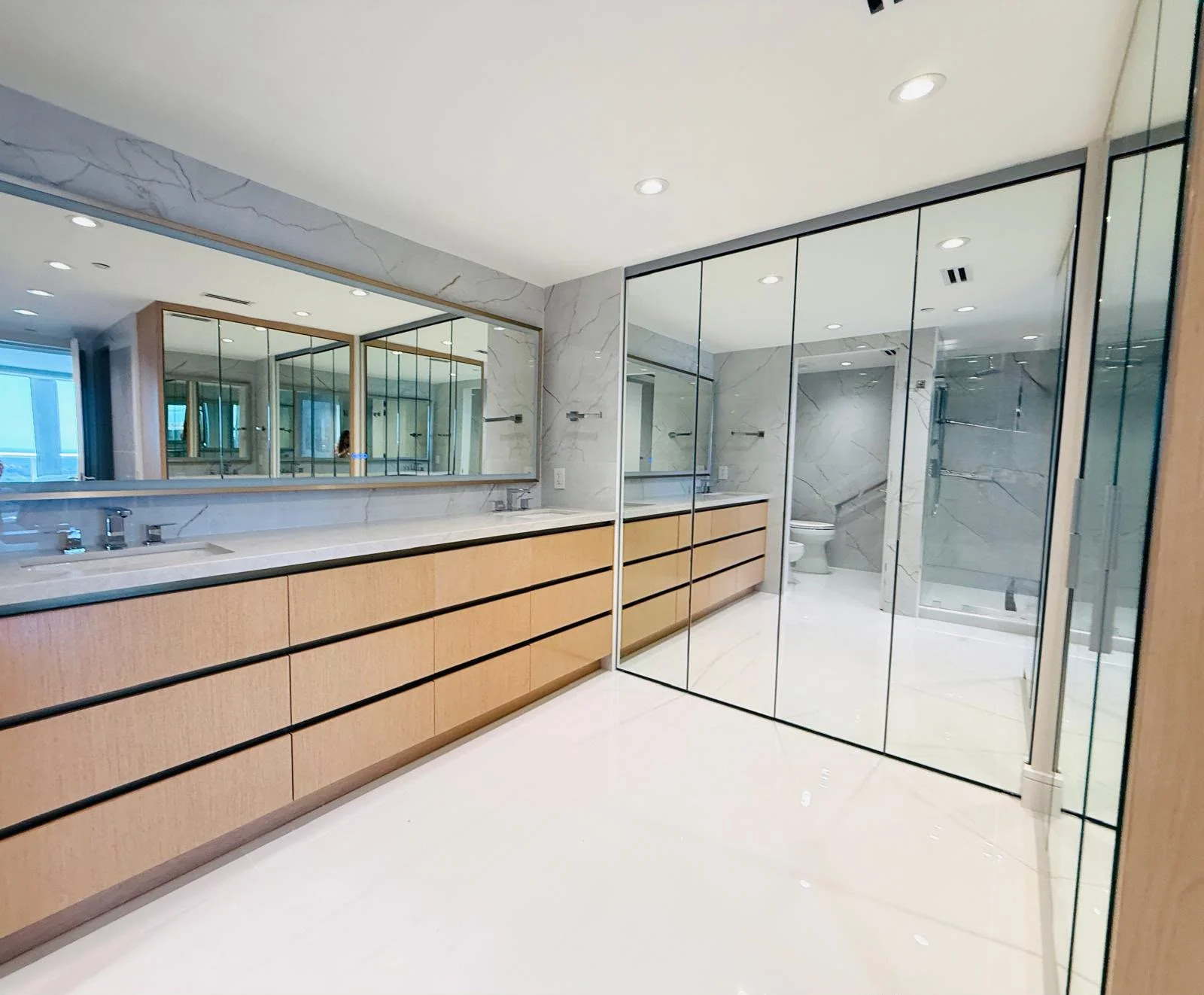 Modern bathroom with oak vanity, frameless glass shower, and marble accents