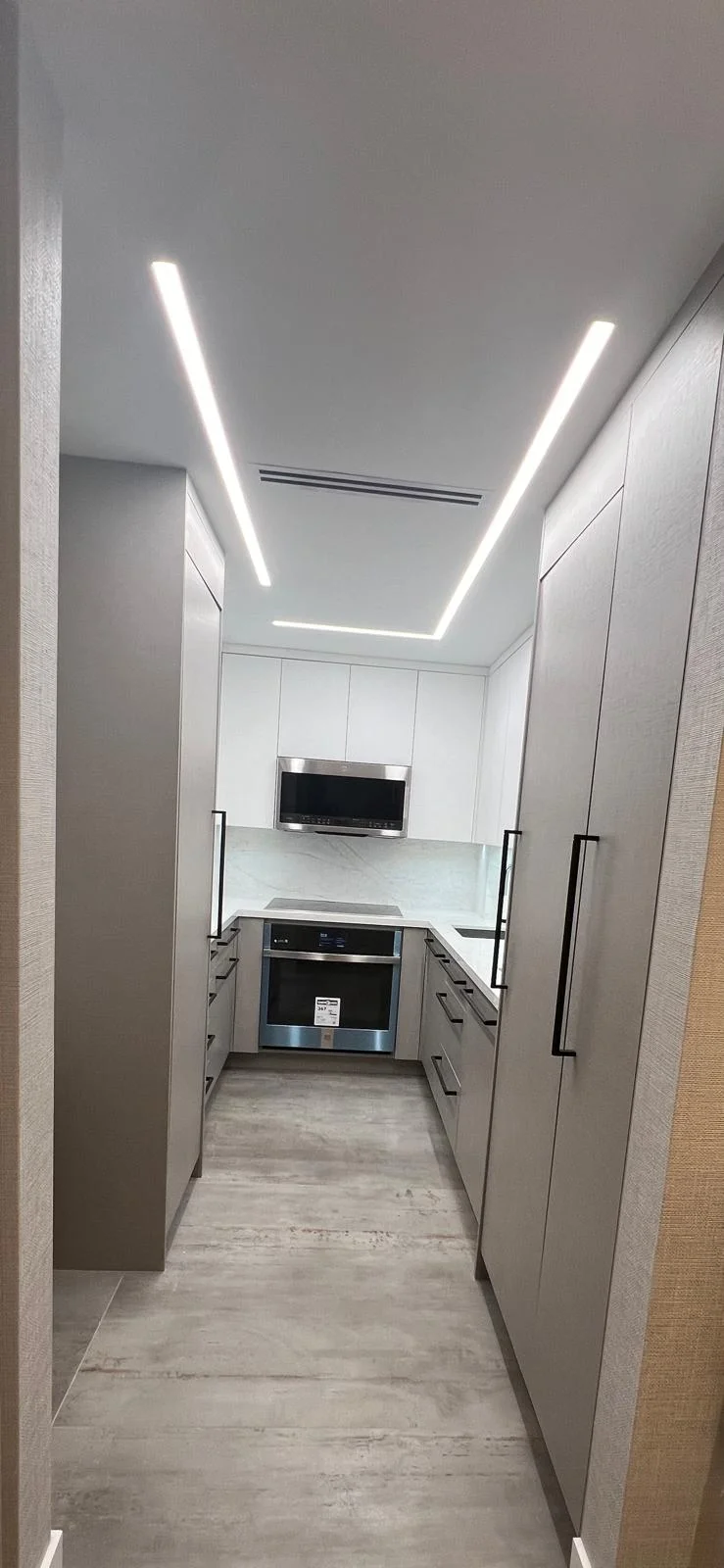Modern white galley kitchen with LED lighting, marble countertop, and stainless steel appliances
