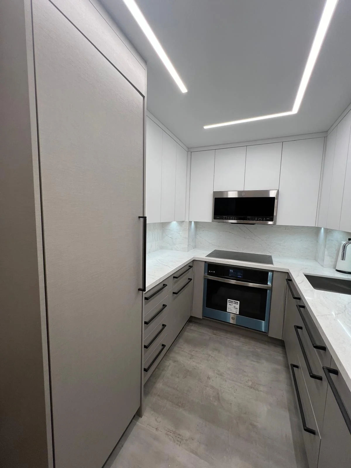 Modern white kitchen with marble backsplash, stainless steel appliances, and geometric LED ceiling lights