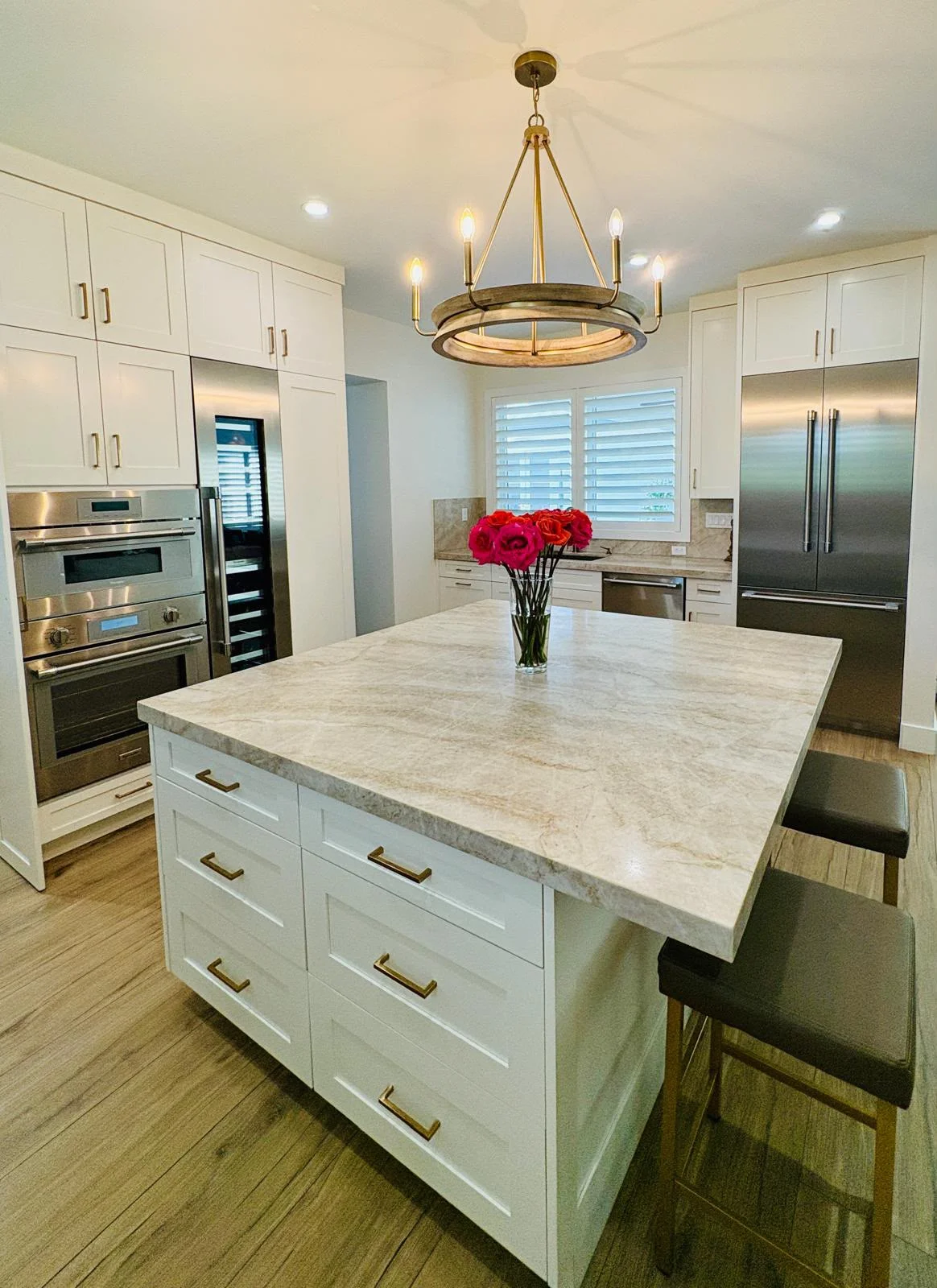 Modern kitchen with white cabinets, marble island, stainless steel appliances, and brass chandelier