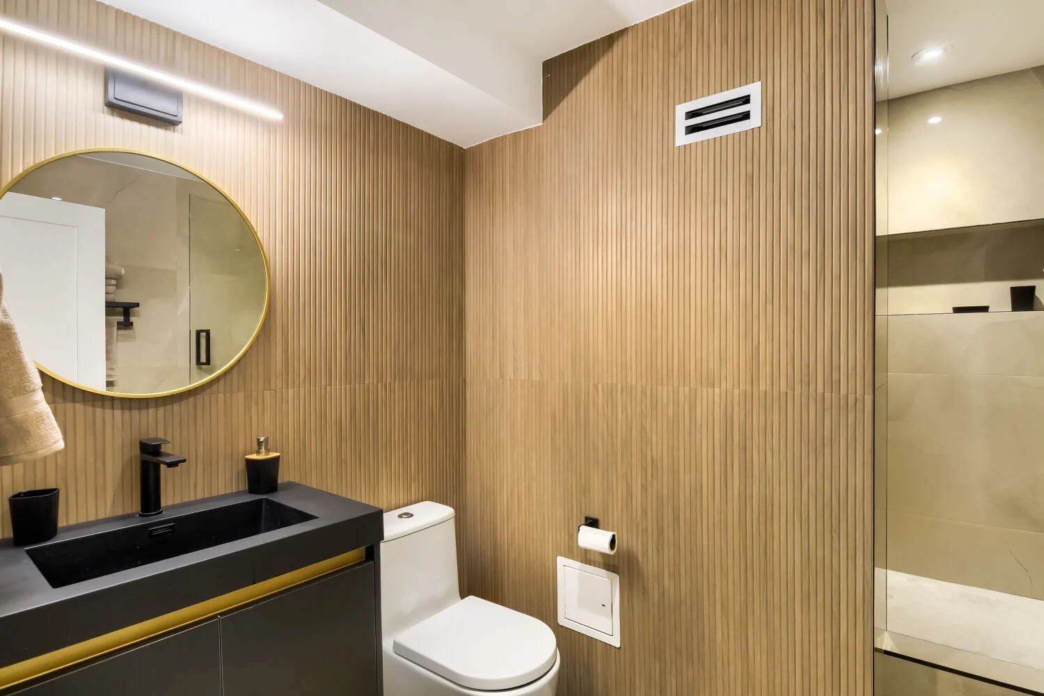 Modern bathroom with wood accent walls, black vanity, and brass mirror
