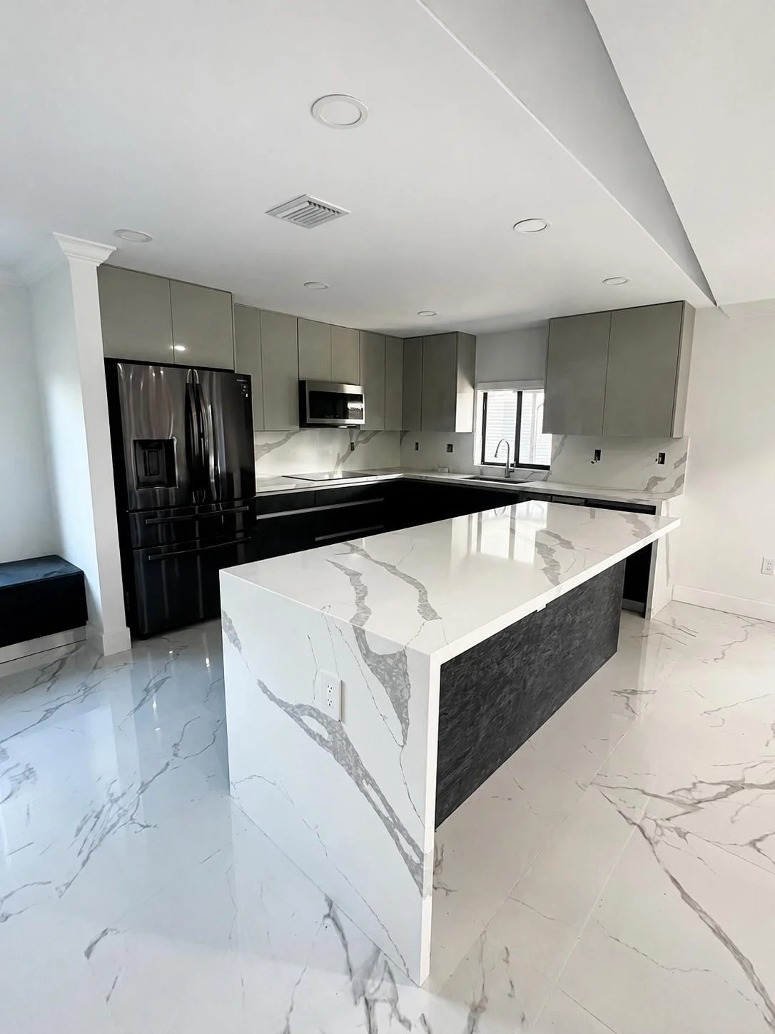 Modern kitchen with gray cabinets, marble island, black appliances, and white marble flooring