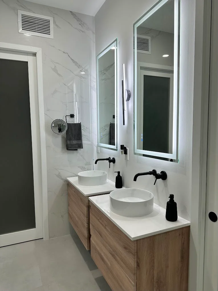 Modern bathroom with double vanity, marble walls, LED mirrors, and black fixtures