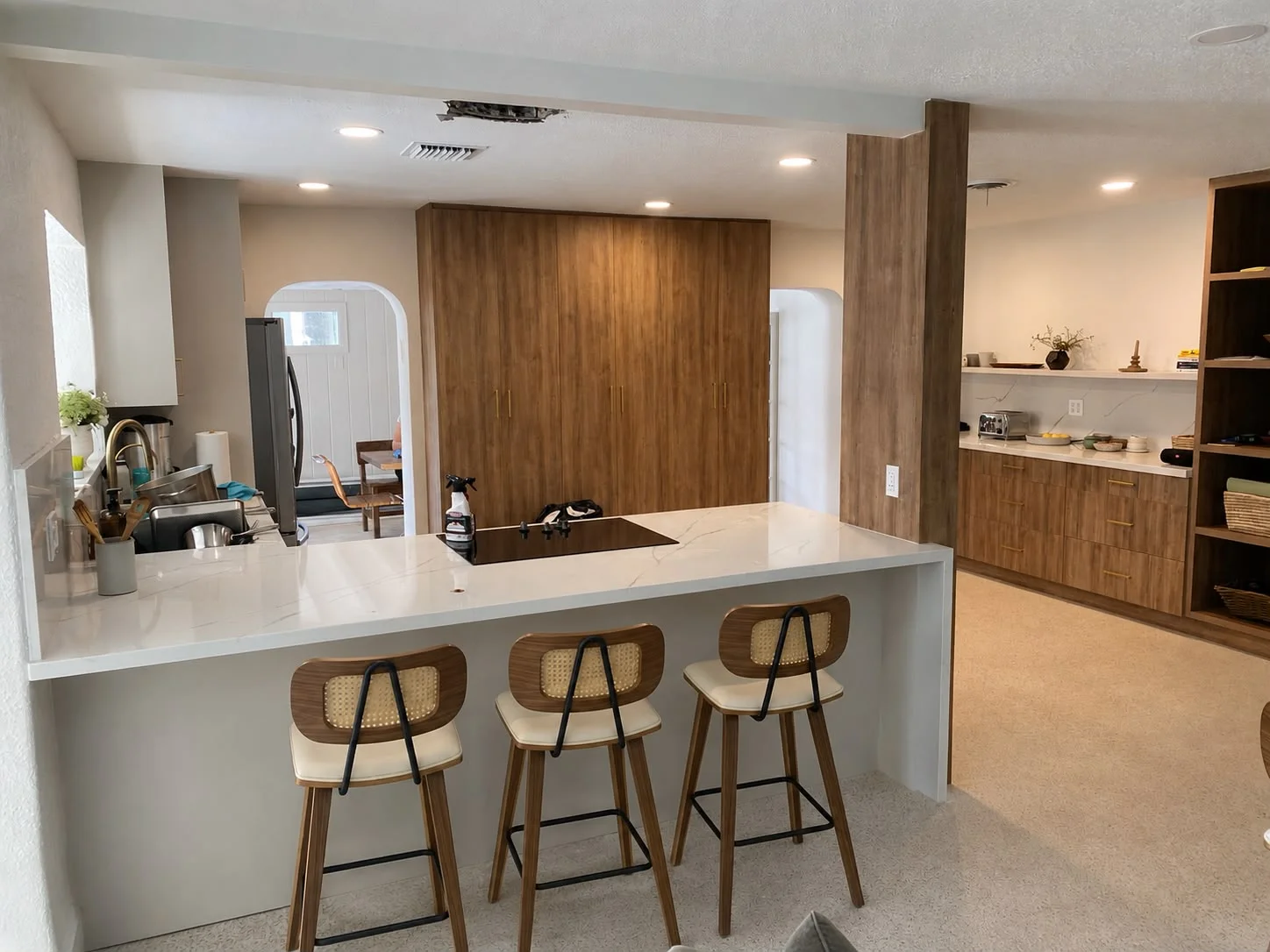 Modern kitchen with walnut cabinets, white island countertop, and three wooden bar stools