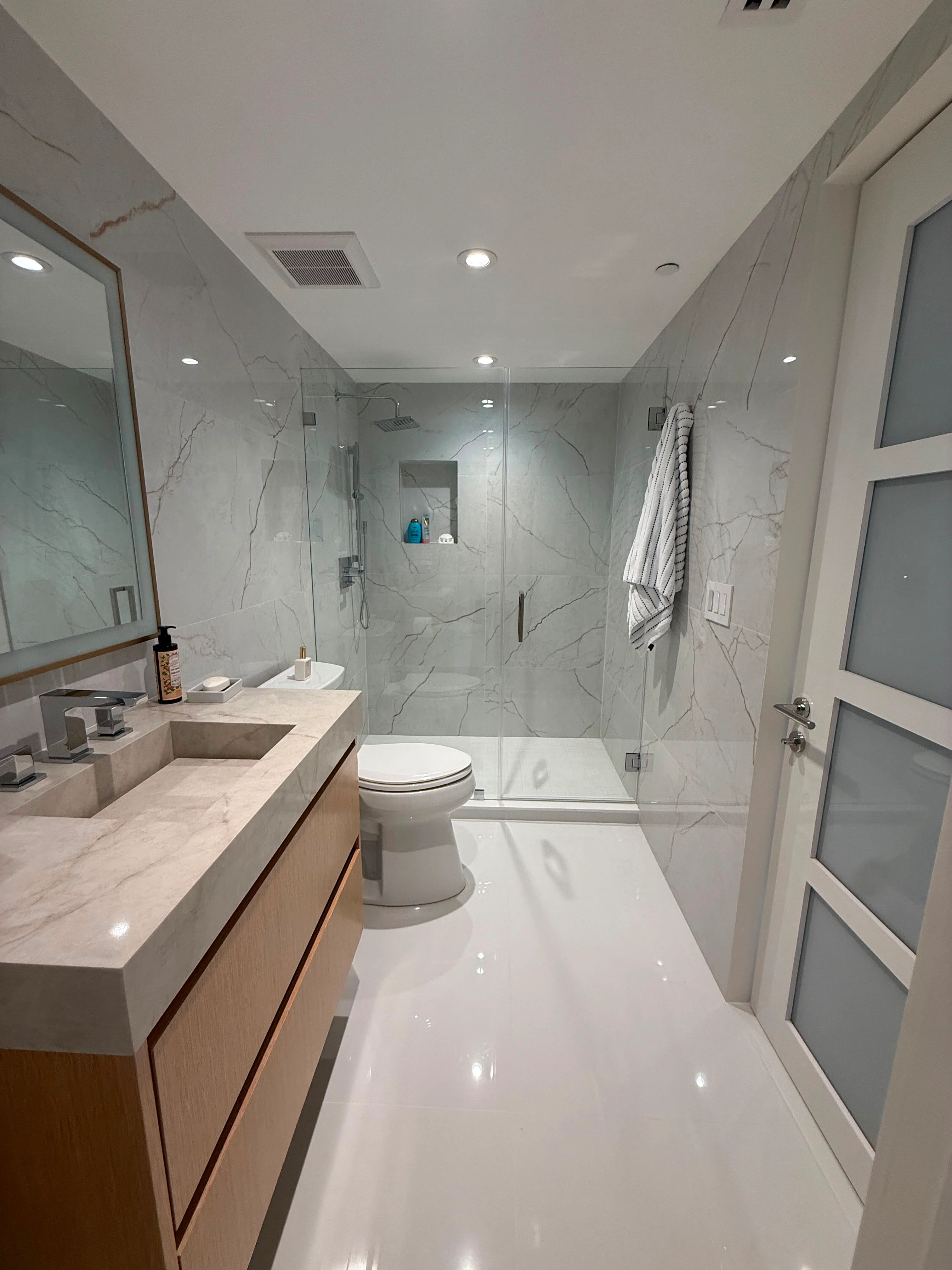 Modern bathroom with white marble tiles, wood vanity, and frameless glass shower enclosure